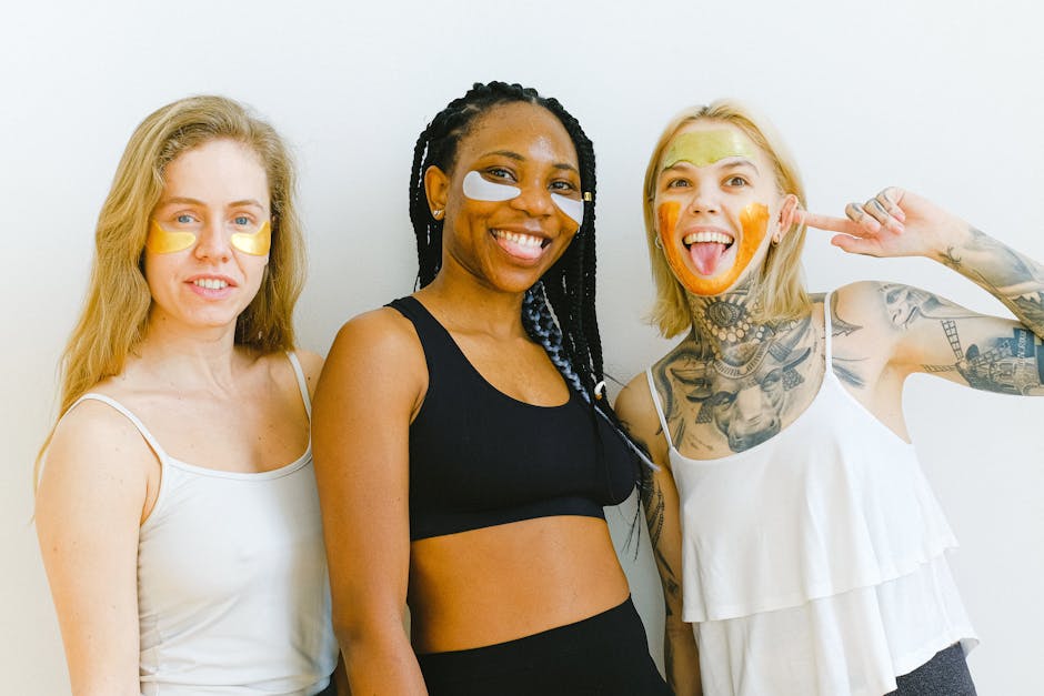 Excited young women smiling and looking at camera while having fun during weekend having beauty procedure with patches and mask