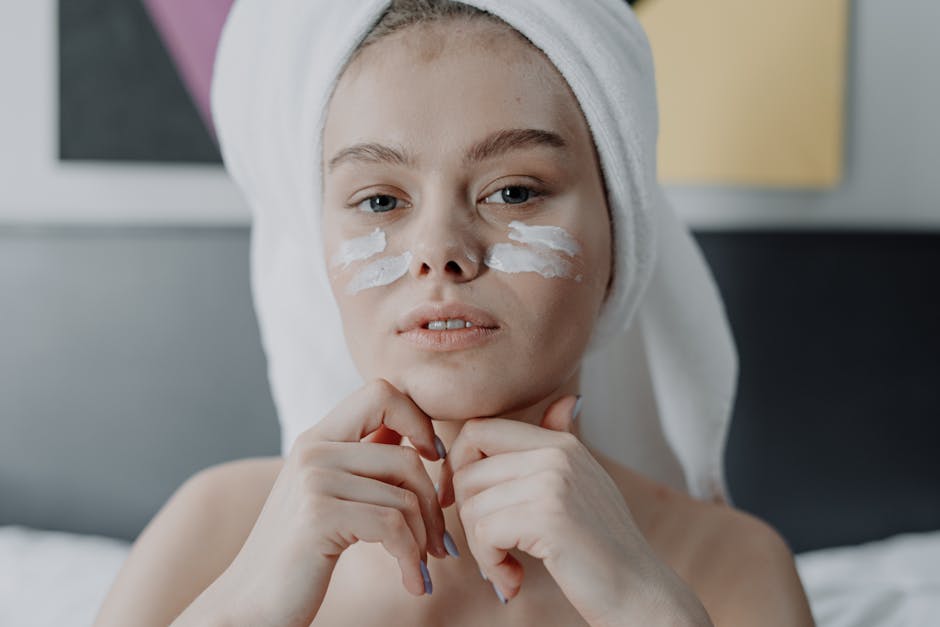 Portrait of a young woman with facial cream, wrapped in a towel, indoor setting