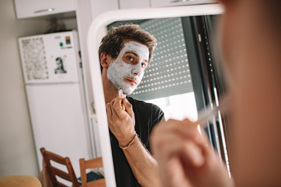 A man applying a face mask while looking into a mirror, emphasizing self-care and grooming