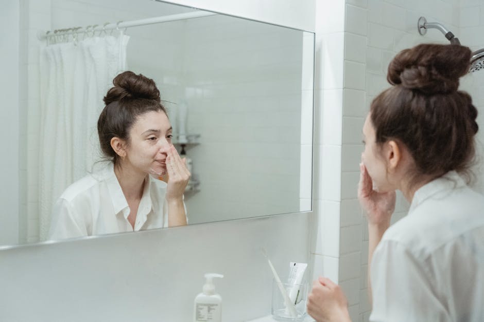 Caucasian woman in bathroom applying skincare product while looking in the mirror