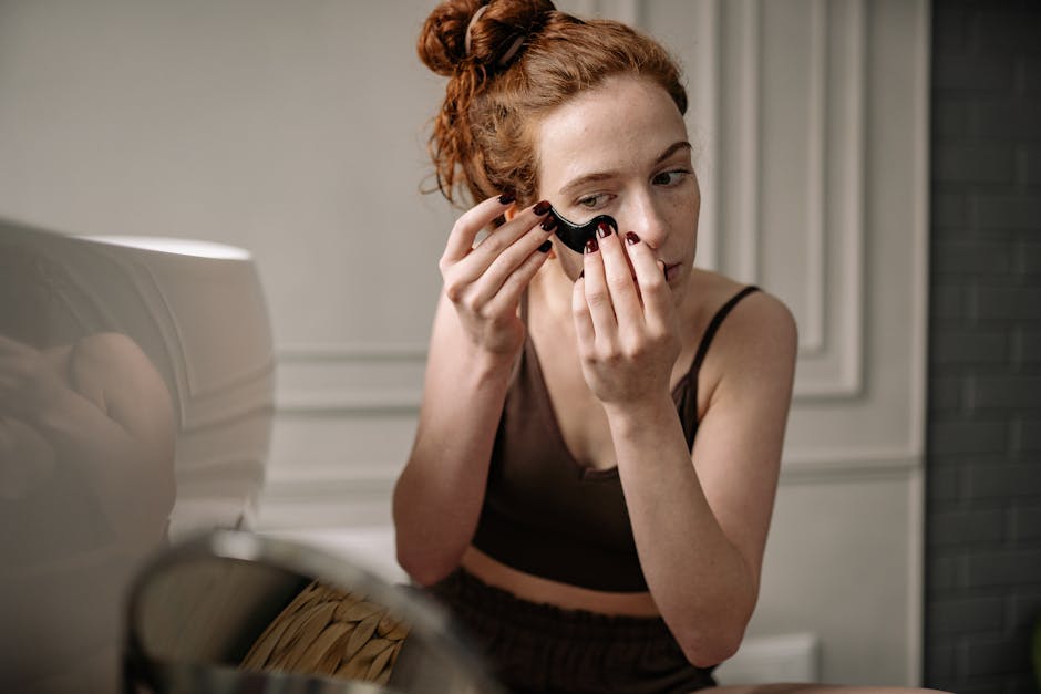 Red-haired woman applying an eye mask for skincare in a cozy room