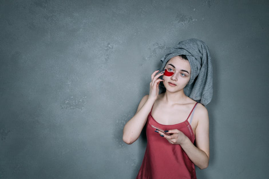 A young woman in a towel applies a rejuvenating under eye patch indoors